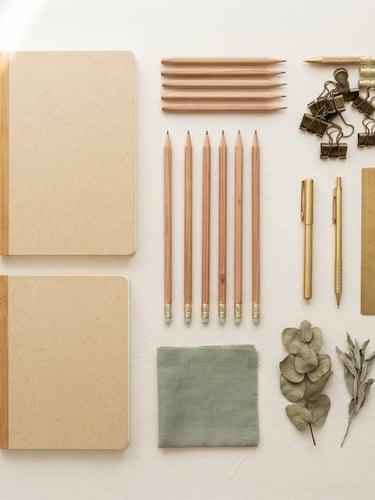 Clean overhead knolling of bamboo-fiber notebooks, cedar pencils, and brass clips on a crisp paper surface, soft natural morning light from the side, muted sage accents, 50mm editorial product photography.