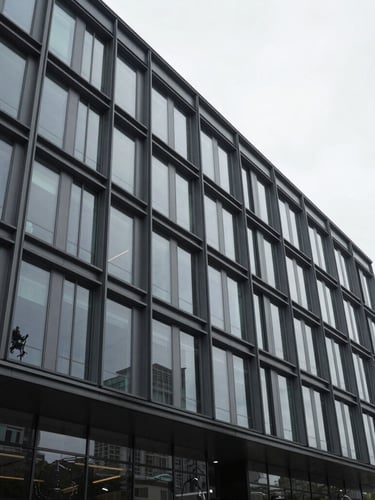 Wide-angle architectural perspective of a modern glass-and-steel commercial building facade under bright overcast daylight, desaturated charcoal tones, sharp focus.