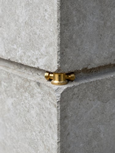 Macro detail shot of a structural brass joint meeting raw concrete, sharp focus, natural diffused daylight, 35mm