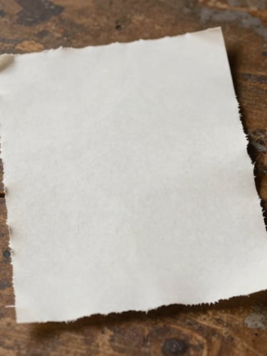 A vertical portrait of raw textured deckled-edge paper resting on a weathered wooden table, soft natural side lighting, minimalist composition.