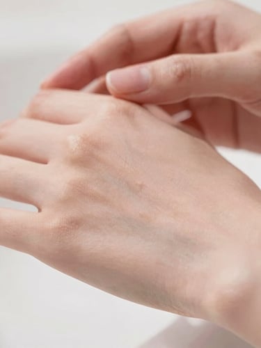 Close-up of glowing clean skin with soft-focus hands, warm diffused daylight, muted dusty rose tones, shallow depth of field
