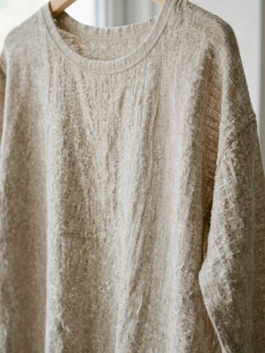 Close-up of a draped oatmeal linen garment on a wooden peg, showing soft rumpled folds and tactile organic texture.
