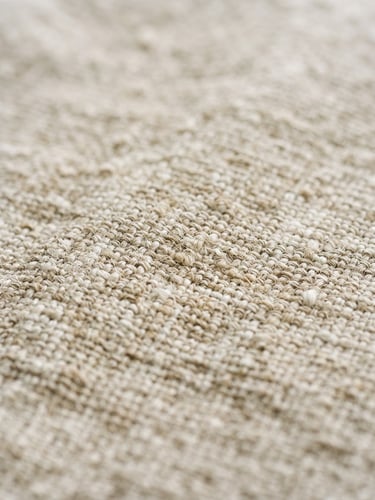 Macro close-up of washed oatmeal linen fabric showing loose, soft, organic weave texture under soft window light.