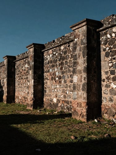 Wide panoramic environmental shot of Jalisco countryside, deep shadows, dramatic natural light hitting a historic stone boundary wall, solemn mood.