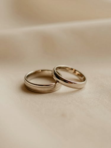 Close-up of elegant wedding rings resting on a soft cream fabric, warm diffused golden light, shallow depth of field, serene editorial photography