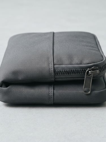Crisp industrial product photography, bright clean studio light, a folded recycled nylon laptop sleeve showing precise double-stitching and heavy-duty metal zippers, neutral cool tones, sharp focus, 35mm