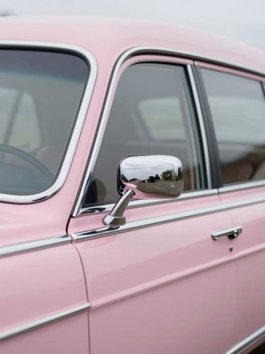 Close-up detail shot of polished chrome accents and the soft pastel pink paintwork of the hearse, shallow depth of field, soft overcast light.