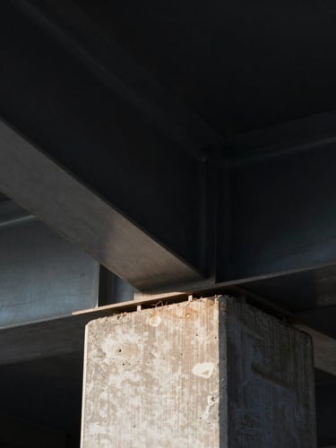 Extreme close-up of structural steel beams and raw concrete foundations under sharp, high-contrast side-lighting, architectural dignity, deep shadows.
