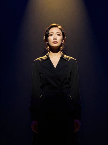 Dramatic stage portrait of a lead actress in dark attire, high-contrast chiaroscuro lighting, deep navy background, warm spotlight gold accent, 35mm film.