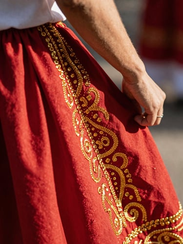 Close-up of hand-embroidered traditional Mexican folkloric dress details, intricate warm gold threads on deep crimson fabric, natural sunlight casting soft shadows