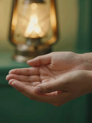 Close-up detail of open hands in quiet contemplation, softly lit by a warm lantern glow, shallow depth of field, rich emerald background.