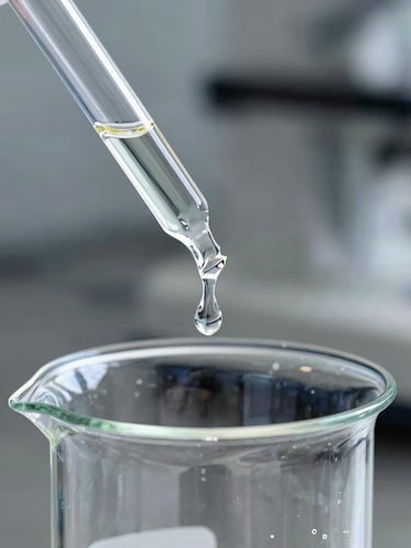 Sharp macro shot of a clear cosmetic ester liquid dripping from a glass pipette into a pristine beaker, cool industrial laboratory lighting, steel background, 35mm
