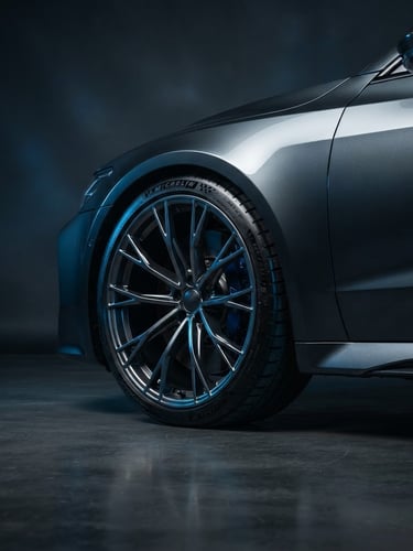 Sleek low-angle shot of a premium sedan showcasing pristine alloy rims and sharp tread patterns, dramatic studio rim lighting, deep charcoal background, 85mm lens