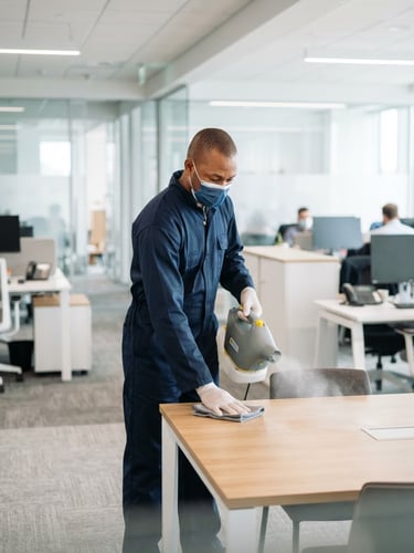 Un technicien de nettoyage guinéen professionnel en uniforme de protection bleu marine, utilisant un pulvérisateur de désinfection technique dans un bureau d'entreprise moderne et lumineux, éclairage commercial blanc et net, 35mm