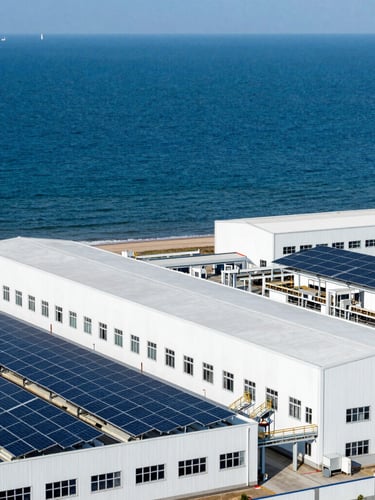 A clean modern industrial facility with solar arrays along a sunny coast, high-contrast deep ocean blues and whites, crisp industrial photography.