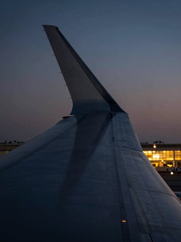 Macro detail of an aircraft wing edge against a deep gradient twilight sky, sharp metallic textures, warm cabin lights glowing in the distance.
