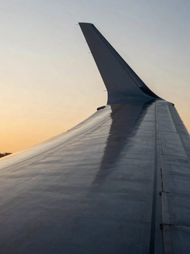 Dramatic architectural close-up of a modern aircraft wing reflecting golden hour sunlight, high-contrast clean lines, premium editorial feel