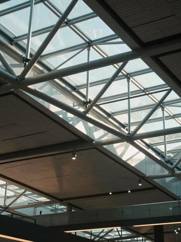 Dramatic high-contrast architectural shot of a modern airport terminal ceiling, steel trusses, cool daylight pouring through glass, cinematic 35mm.