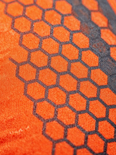 Macro extreme close-up of sublimated athletic fabric weave, showing vibrant neon-orange and charcoal hexagonal patterns integrated into the technical fibers, sharp studio lighting, 85mm lens