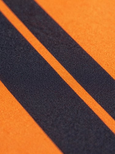 Close-up of vibrant sublimated soccer jersey fabric, deep charcoal and neon-orange patterns, sharp focus on technical fiber pores, bright studio lighting, 85mm lens