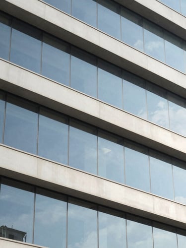 Architectural detail of a modern corporate building facade in Itajaí, clean lines, glass reflections, bright daylight with soft blue shadows, 35mm lens