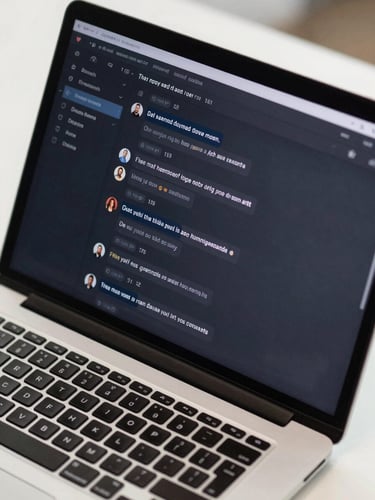 Close-up overhead view of a support dashboard on a laptop screen showing live chat conversations mid-stream, clean dark UI, unread message counts visible, bright even office light