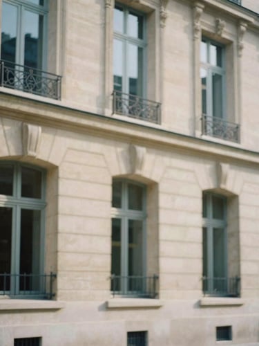 Elegant medium-long shot of classic Parisian limestone building facade, soft diffused daylight, muted navy shadows, shallow depth of field, 35mm