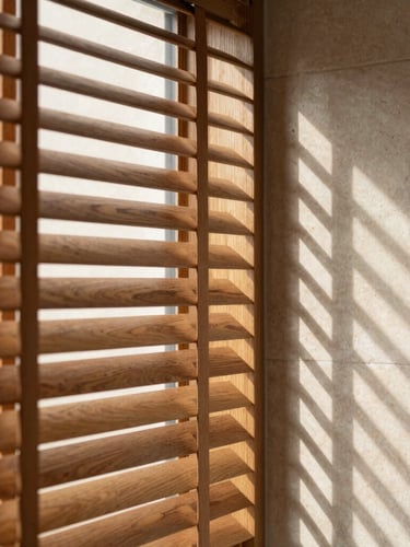 A close-up of a premium timber shutter blind, directional sunlight casting sharp, geometric shadows of the slats onto a minimalist limestone wall, warm editorial style, 35mm lens.