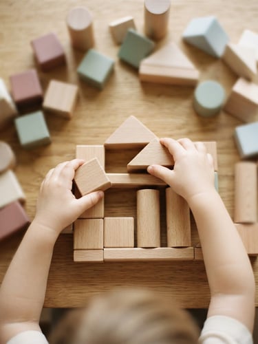 Overhead flat-lay of a child's hands carefully arranging smooth wooden blocks on an ivory table, soft natural morning light, shallow depth of field, warm editorial photography