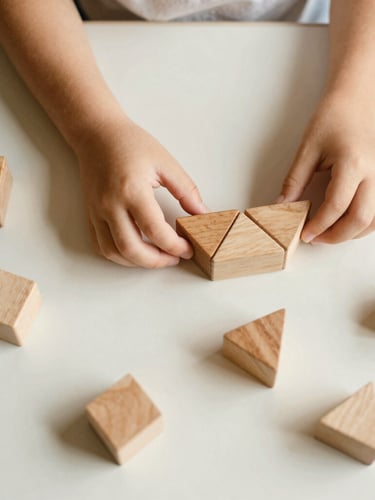 Overhead flat-lay of a child's hands carefully arranging warm wooden geometric blocks on an ivory table, soft natural north-facing daylight, shallow depth of field