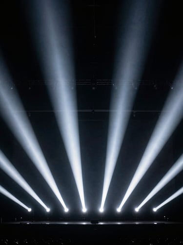 Wide dramatic angle of a massive stage lighting installation, sharp beams of white light cutting through dark atmosphere, deep black background, high contrast, 35mm