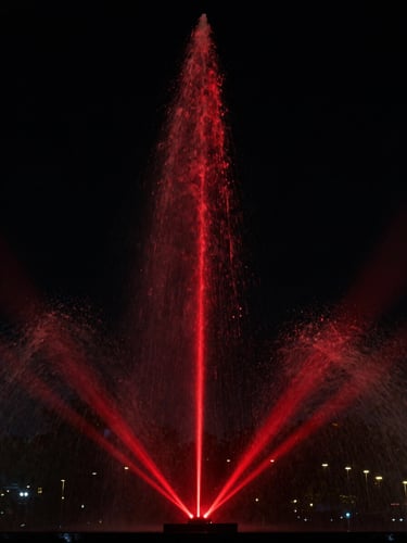 Dramatic low-key photograph of a synchronized musical fountain nozzle, sharp theatrical red light beam cutting through water droplets, dark night sky background, 35mm