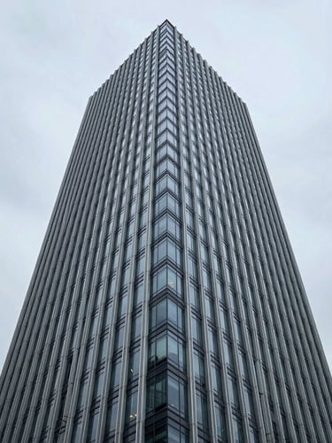 Symmetrical wide-angle architectural shot of a modern corporate skyscraper exterior, steel and glass facade, cool overcast daylight, sharp clean lines, negative space on the left.