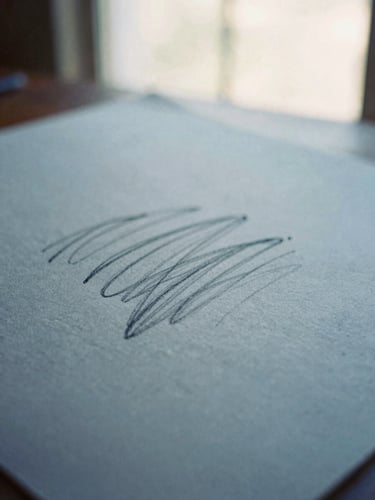 Close-up of physical art medium, charcoal strokes on thick textured warm gray paper, soft diffused window light, shallow depth of field, 35mm