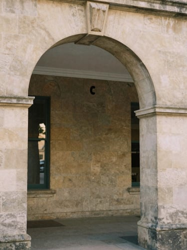Soft natural daylight reflecting on the stone archway of a historic community center, warm editorial photography, muted earth tones.