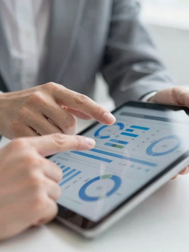 Close-up of professional hands reviewing risk management metrics on a tablet screen, bright natural daylight, clean gray and slate blue tones, shallow depth of field.
