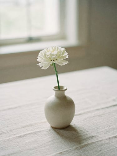 Close-up of a minimalist wedding table setting, raw linen, single-stem white floral in a ceramic vase, soft natural window light, editorial 35mm photography
