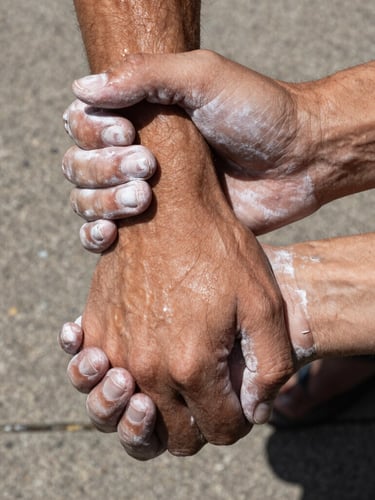 Extreme close-up of chalked hands firmly gripping a partner's wrist, high-contrast harsh daylight, visible sweat and physical strain, raw concrete background.