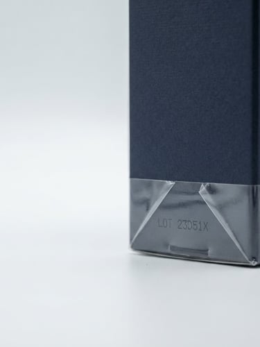 Macro shot of a high-end perfume box with a visible factory seal and batch number, clean studio light, crisp details, white and soft gray background, 50mm lens, right third of the frame.