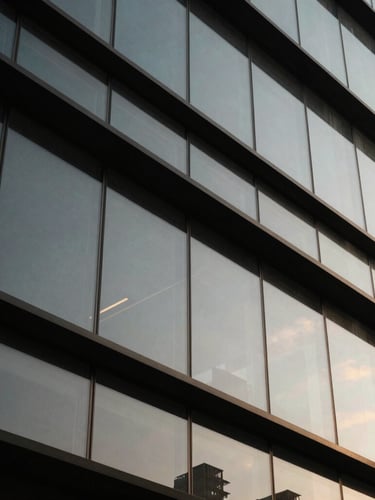 Close-up of clean structural glass joints and black steel frames in a modern building lobby, sharp architectural lines, dramatic side lighting, desaturated tones