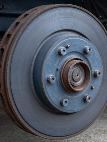 Macro shot of a heavy-duty truck brake drum, metallic texture, crisp industrial daylight, deep slate blue tones, sharp focus, 35mm