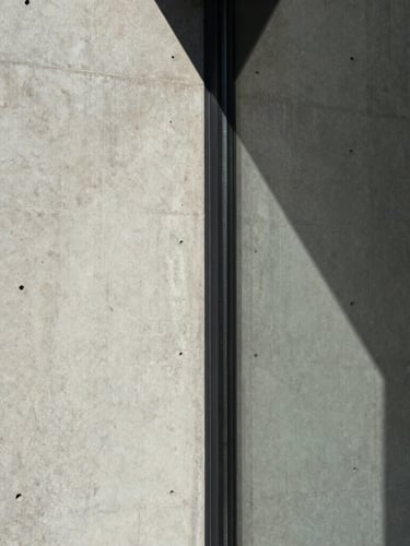 Extreme close-up of a raw concrete wall meeting a clean glass panel, sharp natural light casting a geometric shadow, architectural detail, desaturated, 35mm