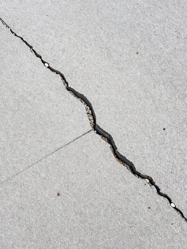 Top-down detail shot of pavement wear and concrete cracking on an overcast day, sharp focus, technical inspection context.
