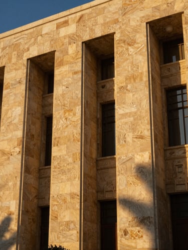 Low-angle heroic shot of a modern Syrian stone facade at golden hour, deep shadows, rich gold tones, elegant architectural photography.