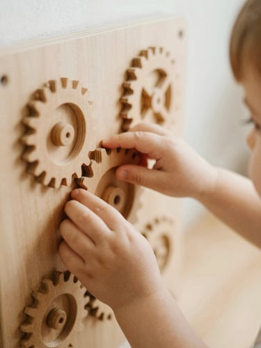 A close-up shot of a child's hands gently exploring a wooden sensory tactile wall with textured gears, soft warm indoor lighting, shallow depth of field, 35mm