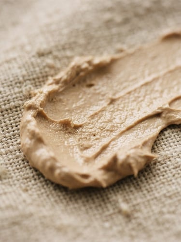 Macro close-up of a thick cream swatch on textured linen, soft natural daylight, warm sand tones, 35mm film grain.