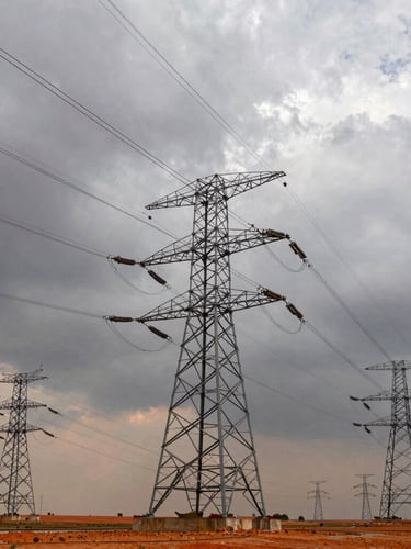 Wide-angle environmental shot of high-voltage transmission lines stretching across a dramatic overcast sky with metallic structures