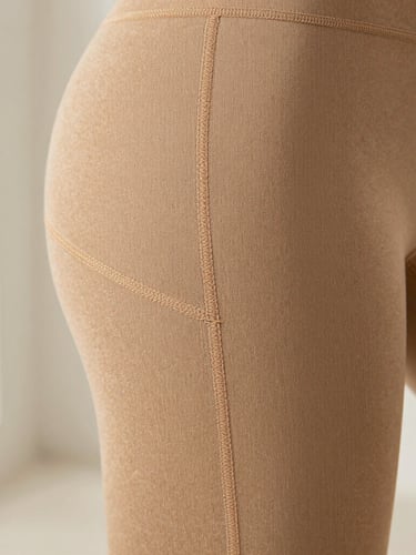Close-up macro shot of flat-lock stitching on a warm-sand colored activewear legging, highlighting the precise, seamless construction and fabric texture, soft natural daylight, minimalist background, shallow depth of field.