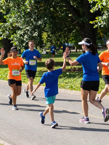 A family high-fiving during a local fun run, bright natural daylight, vibrant active mood, outdoor park setting, 35mm.
