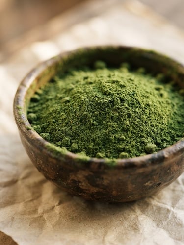 Macro shot of vibrant green moringa powder in a rustic clay bowl, soft afternoon side-light, unbleached parchment background, 35mm photography